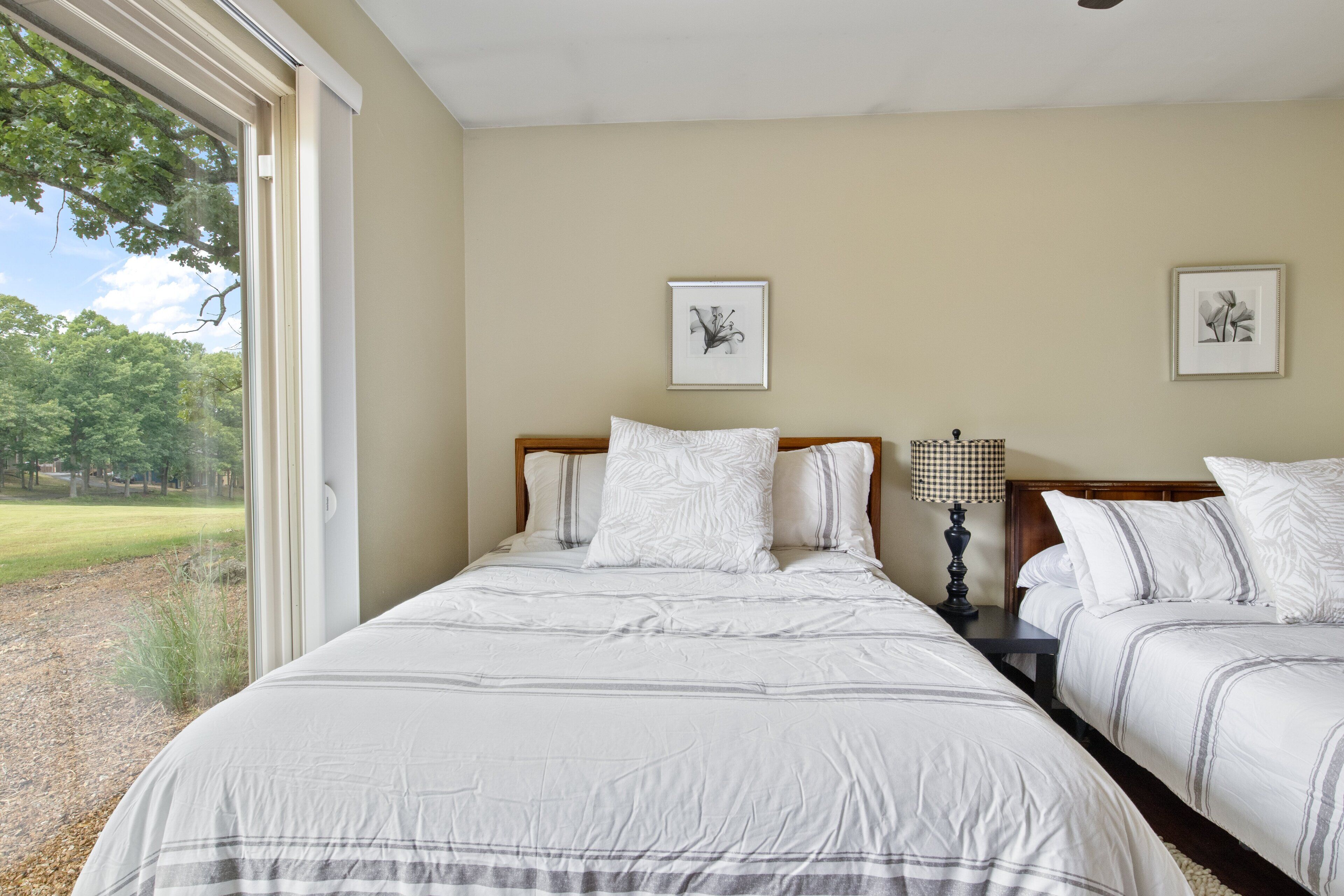 A bedroom with two beds, a large window, and a view of a grassy area.