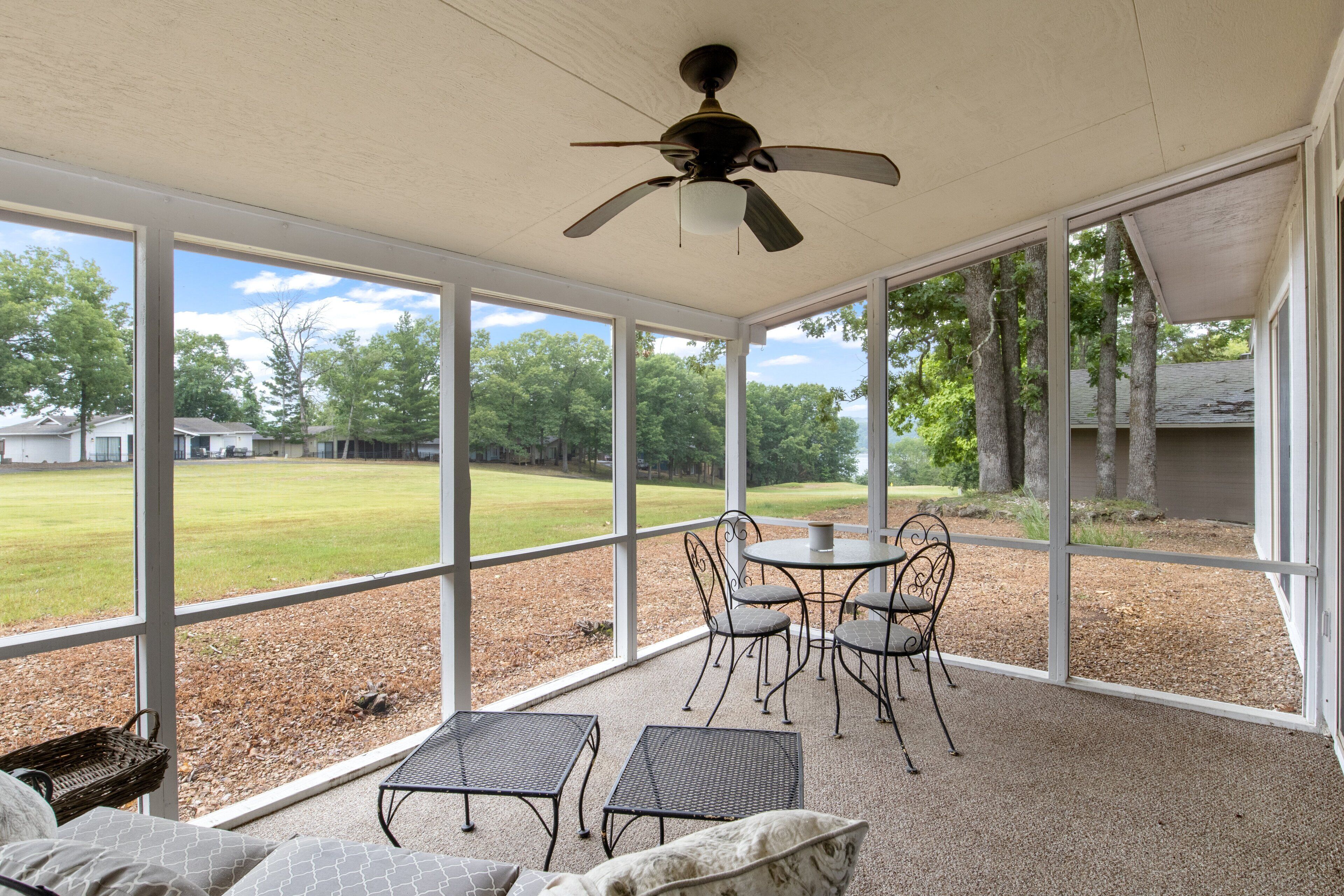 Un patio couvert avec un ventilateur de plafond, une table avec des chaises et une vue sur une cour verdoyante.