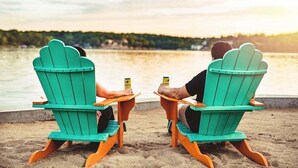 Two people sitting on green Adirondack chairs facing a body of water with a forested shoreline in the background. - Perfect Resort Retreat Close to Everything (Osage Beach)