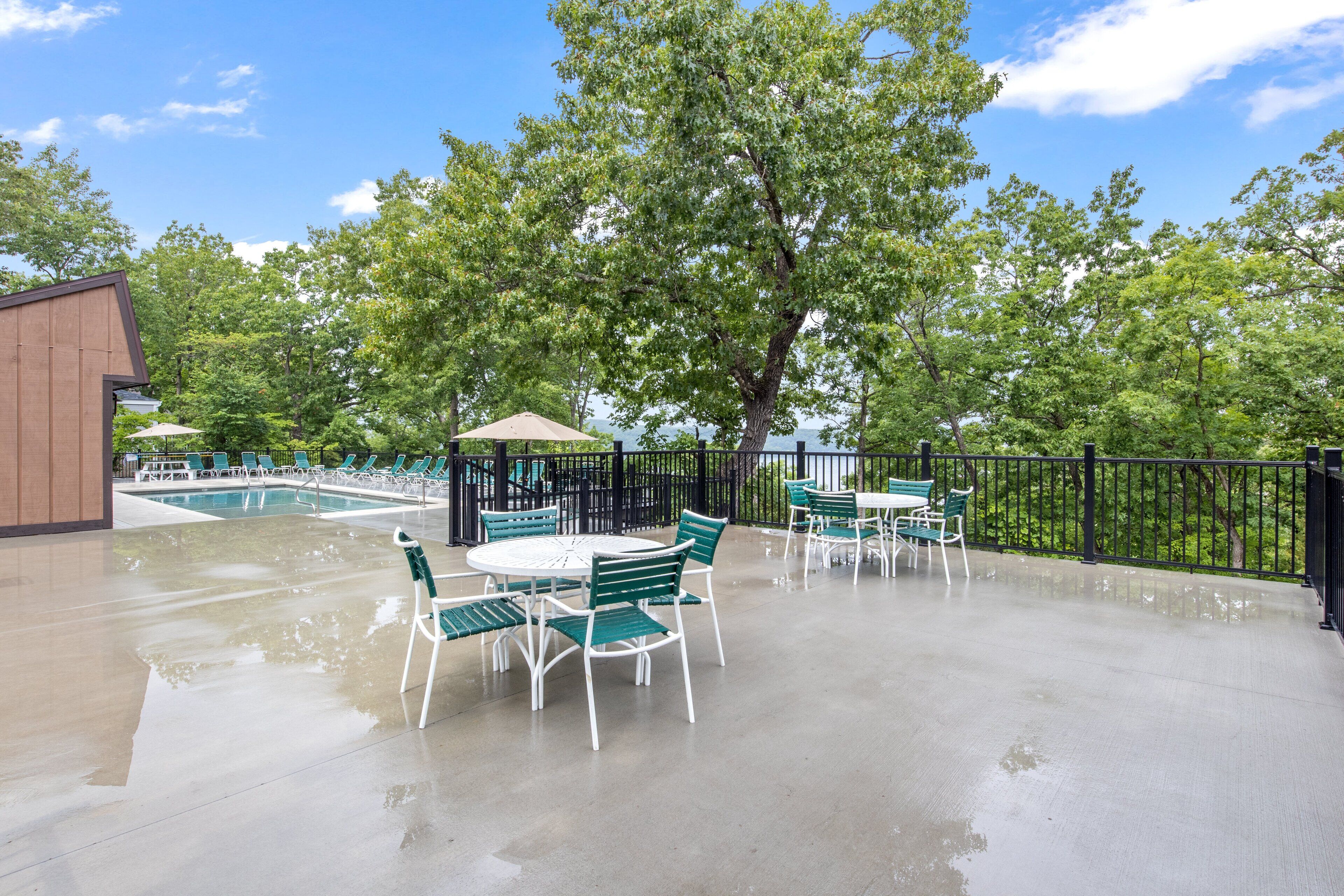 Eine Terrasse im Freien mit Pool, grünen Stühlen und einem Tisch.