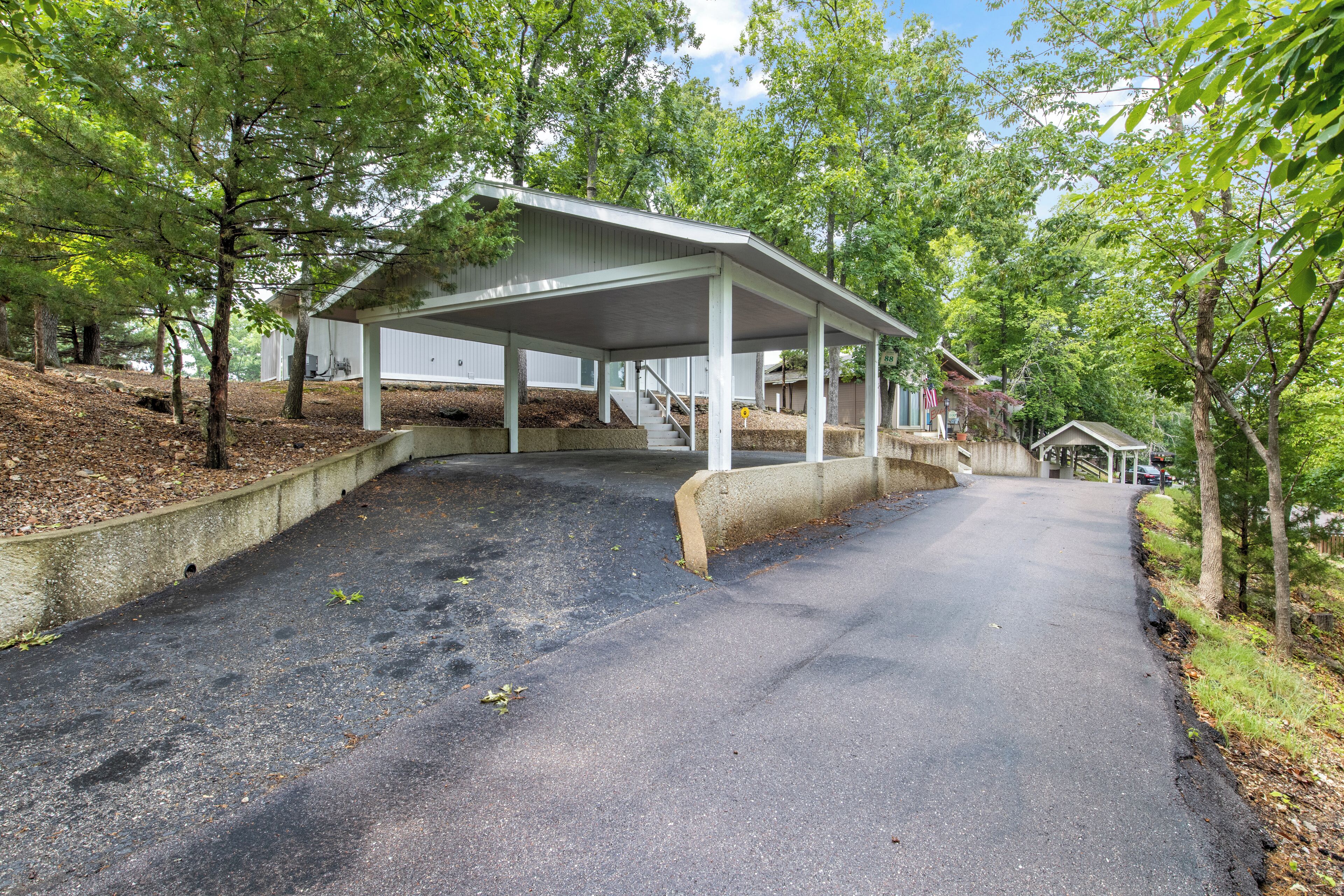 A covered parking area with a concrete ramp leading to a building with a white exterior.