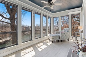 A sunroom with large windows, a ceiling fan, and a view of a tree and a river. - Spacious Home & Lake Access, Lake Views Throughout (Lake Ozark)