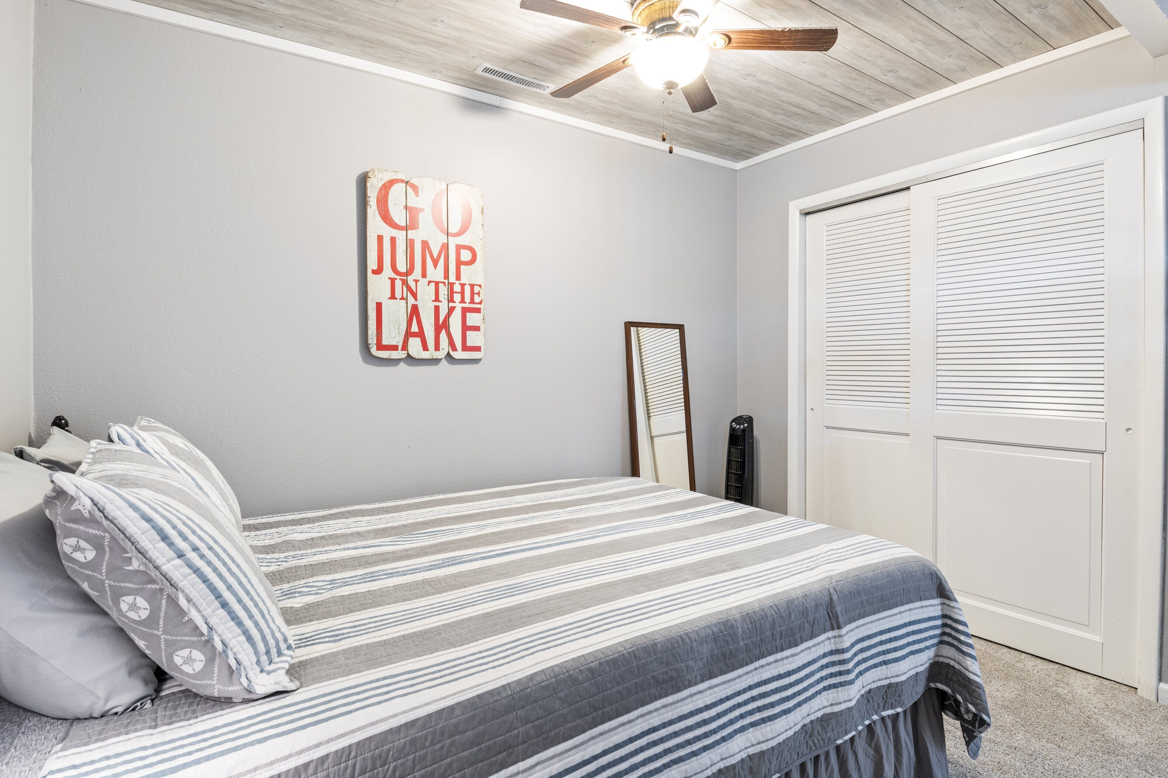 Quarto com cama, travesseiros, ventilador de teto, placa na parede, espelho e armário.