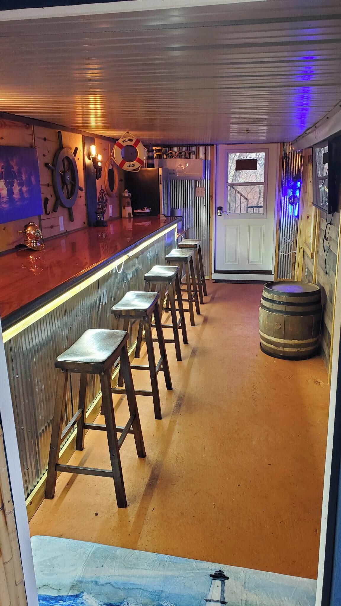 A bar area with stools, a wooden barrel, and nautical-themed decor.