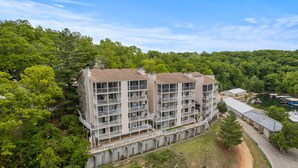 A multi-story building with balconies, surrounded by dense greenery and a clear sky. - Great Views and Pool Next to Docknockers! (Lake Ozark)