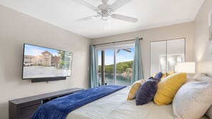 A bedroom with a bed, a TV mounted on the wall, a ceiling fan, a balcony with a view, and a large mirror. - Great Views and Pool Next to Docknockers! (Lake Ozark)