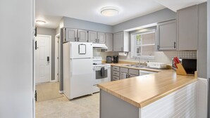 A modern kitchen with grey cabinets, a white refrigerator, a stove, and a wooden countertop. - Great Views and Pool Next to Docknockers! (Lake Ozark)
