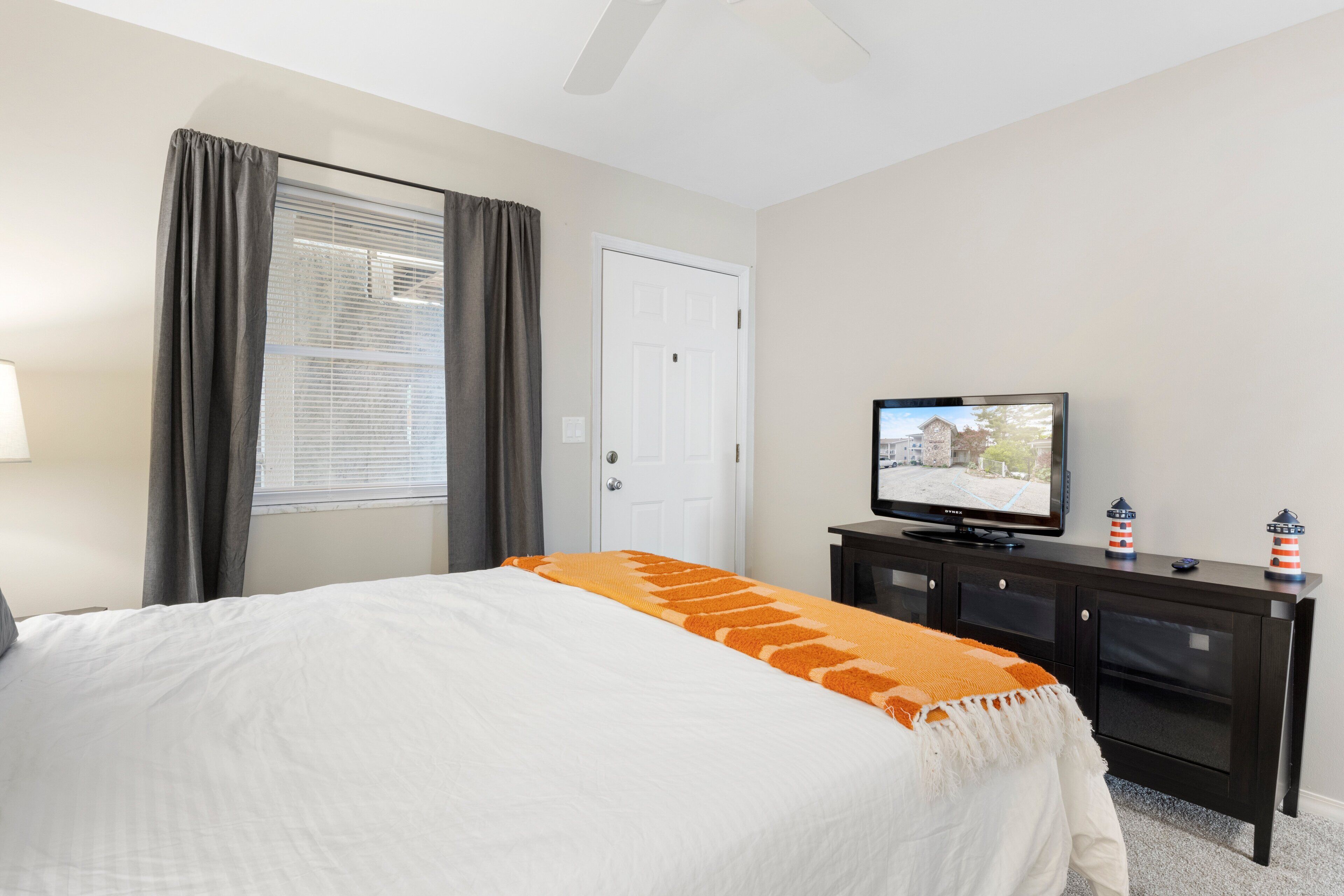 A hotel room with a bed, a television, a dresser, and a window with curtains.