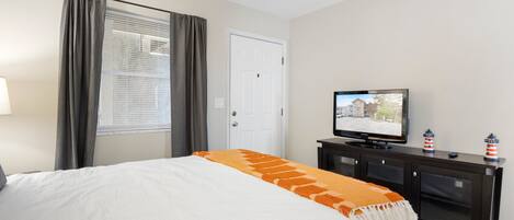 A hotel room with a bed, a television, a dresser, and a window with curtains.