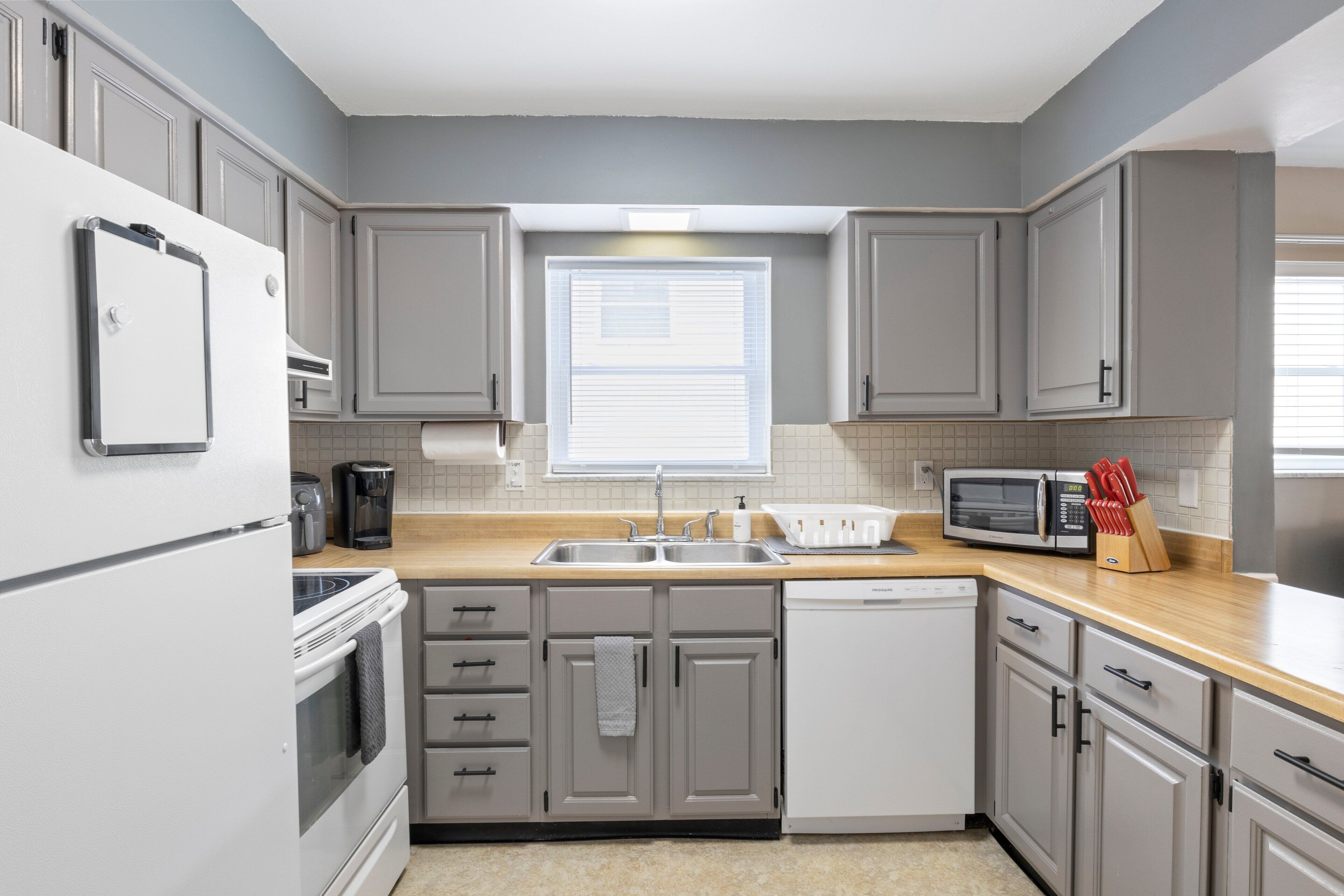 A modern kitchen with grey cabinets, a stainless steel sink, a microwave, and a dishwasher.