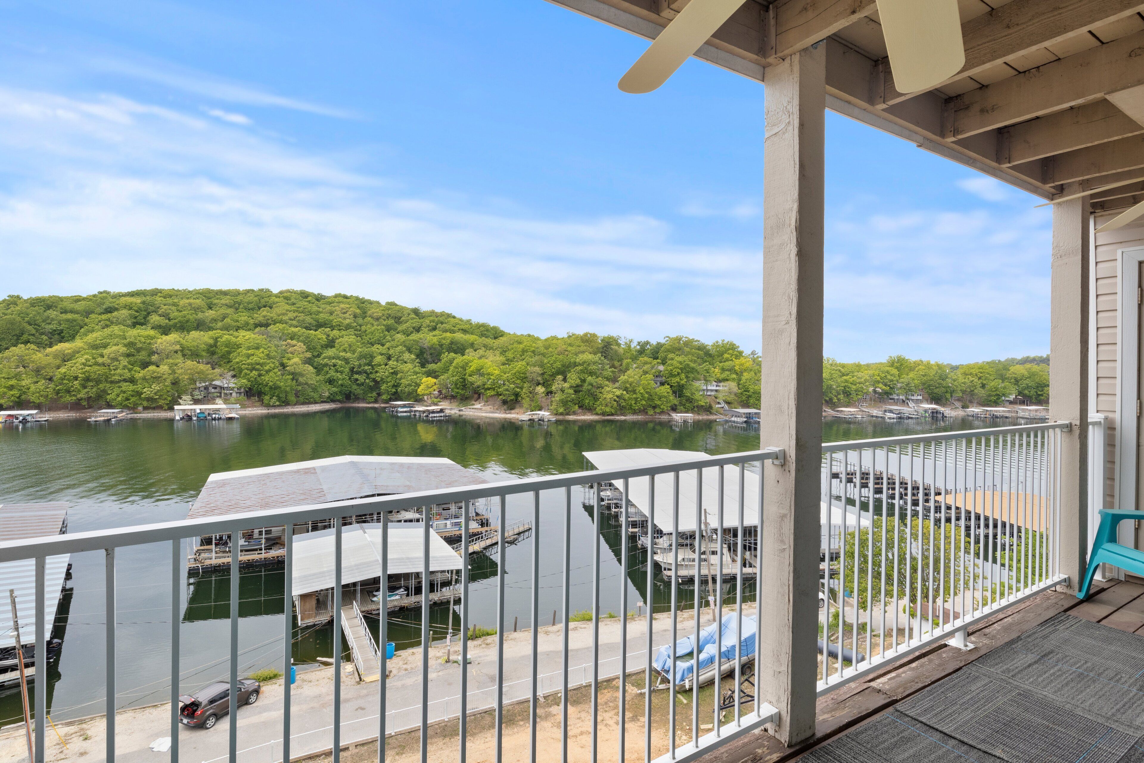 A view from a balcony overlooking a lake with boats, a dock, and a forested hill.