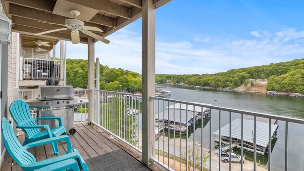 A covered deck with outdoor seating, a grill, and a view of a lake with boats and docked vehicles. - Great Views and Pool Next to Docknockers! (Lake Ozark)