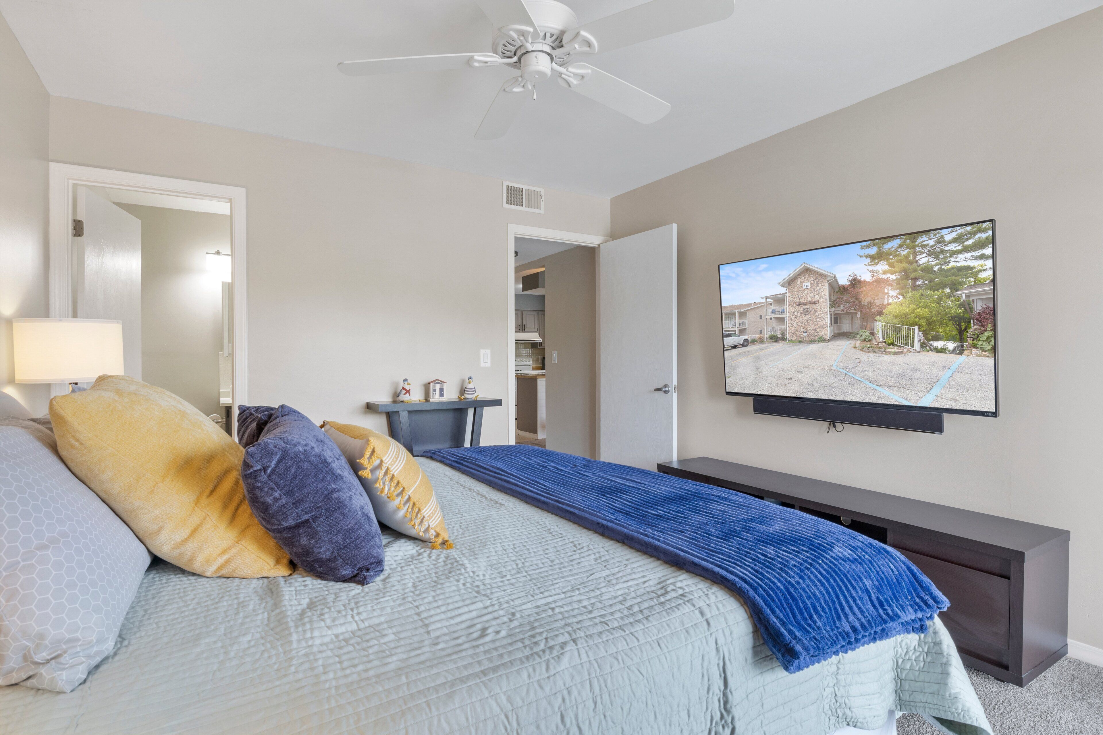 Une chambre à coucher avec un lit, un téléviseur fixé au mur, un ventilateur de plafond et une vue sur l’extérieur.