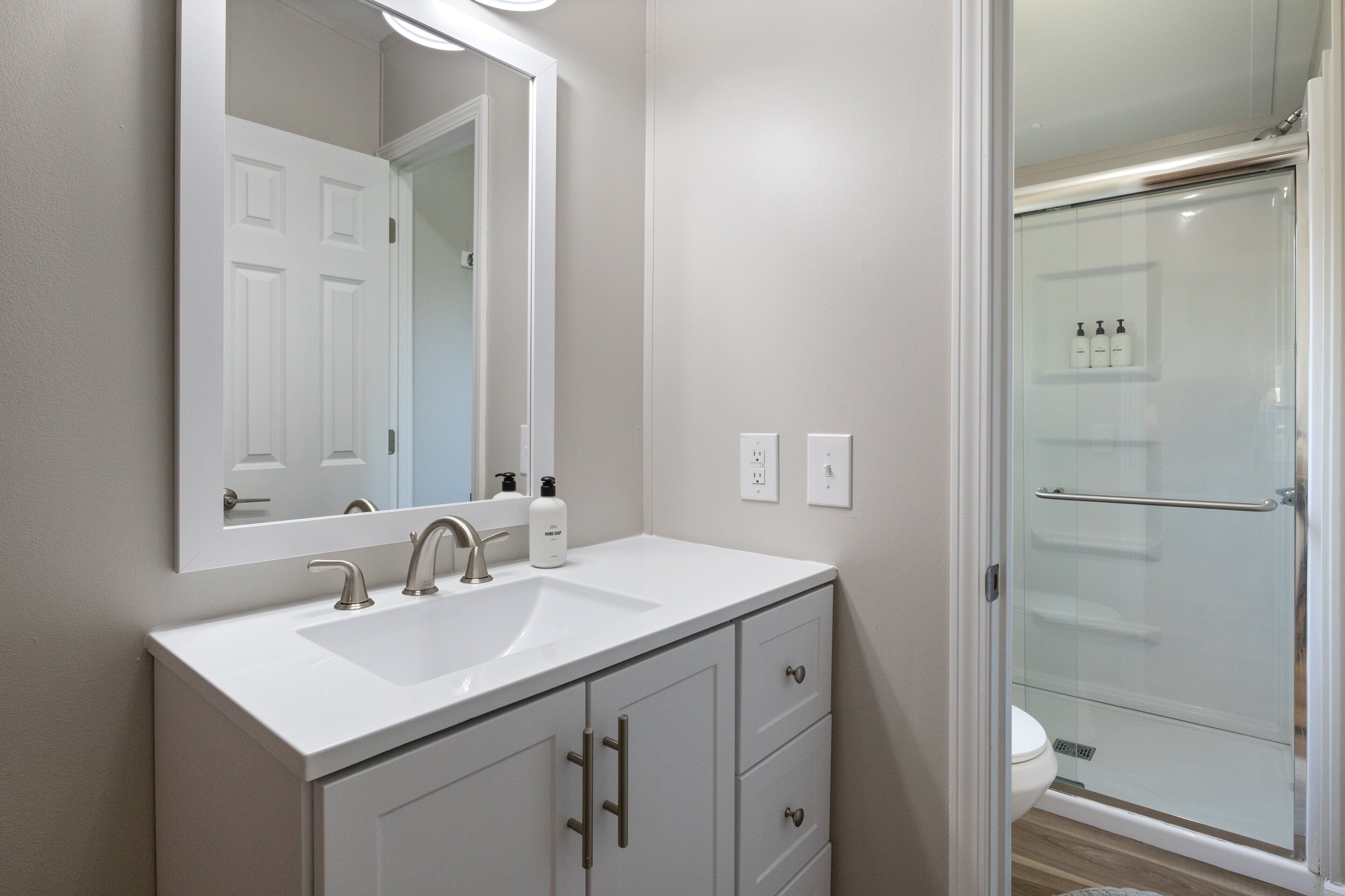 Une salle de bain avec un lavabo blanc, un miroir et une cabine de douche en verre.