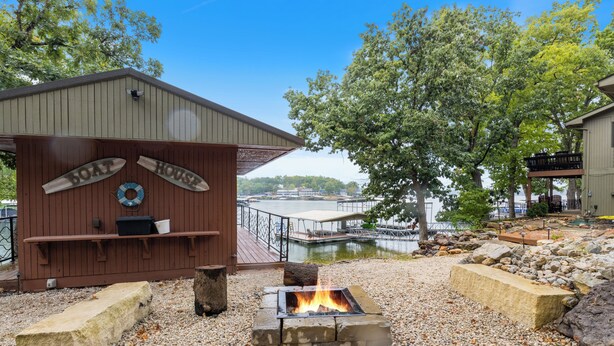 A wooden boat house with a fire pit and a dock extending into a body of water. - Game Room, Dock Life, Fire Pit & Hot Tub! (Lake Ozark)