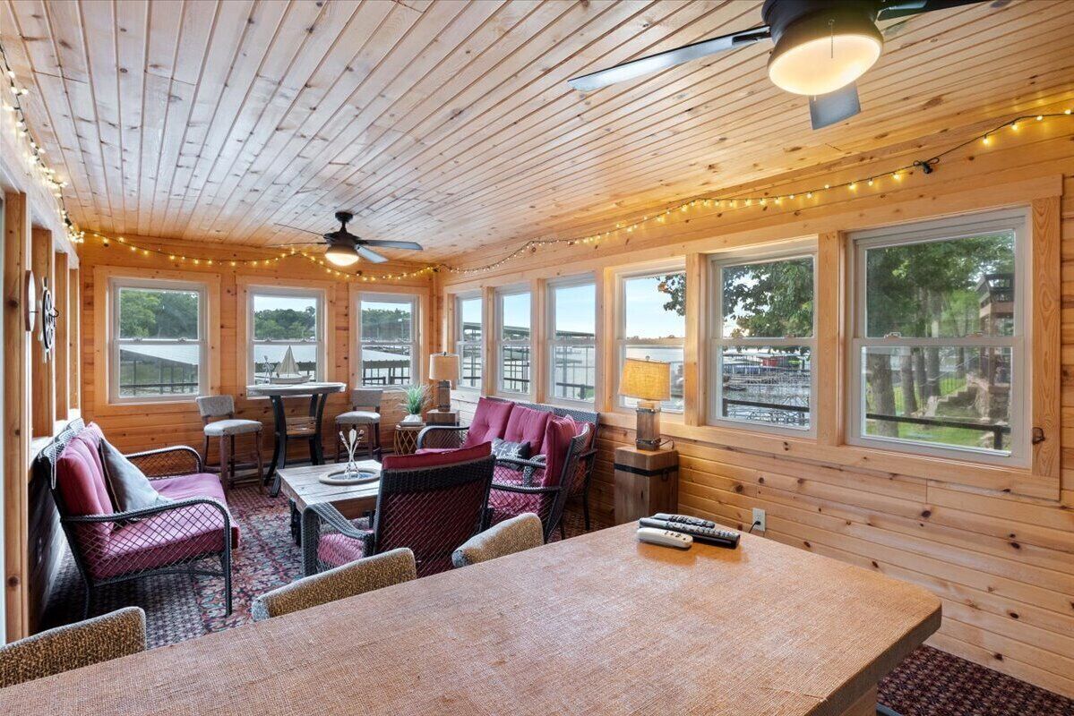 Un acogedor interior de cabaña con paredes de madera, ventanas amplias, una zona de comedor y una sala de estar con mesa y sillas.