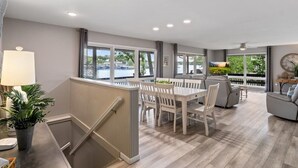 A spacious living area with a dining table, chairs, and a sofa. There are large windows providing views of the outdoors. - Game Room, Dock Life, Fire Pit & Hot Tub! (Lake Ozark)