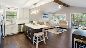 A modern kitchen with white cabinets, a central island, and a dining area with a sofa and coffee table. - Spacious, Central Location, Fire Pit, Boat Slip (Lake Ozark)