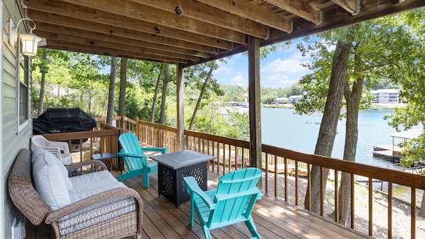 A covered outdoor deck with wicker furniture, a grill, and a view of a lake. - Spacious, Central Location, Fire Pit, Boat Slip (Lake Ozark)