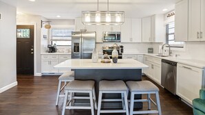 A modern kitchen with white cabinets, stainless steel appliances, and a central island with bar stools. - Spacious, Central Location, Fire Pit, Boat Slip (Lake Ozark)