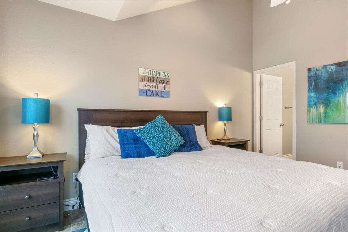 Quarto com cama grande, duas mesas de cabeceira com abajures, cabeceira de madeira e um letreiro fixado na parede.
