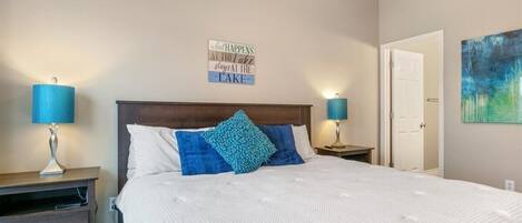 Quarto com cama grande, duas mesas de cabeceira com abajures, cabeceira de madeira e um letreiro fixado na parede.