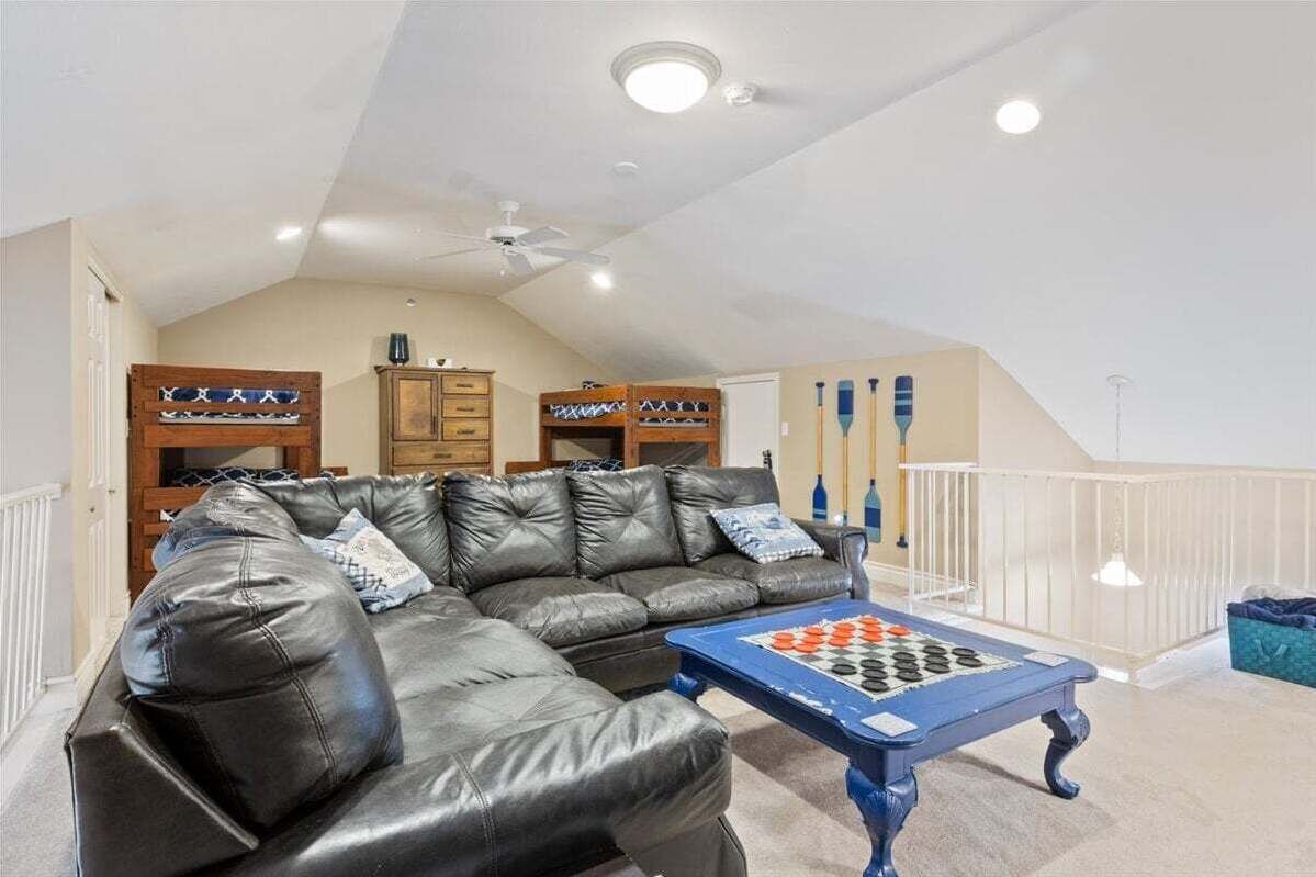 Un salon avec un canapé en cuir noir, une table basse bleue ornée d’un jeu d’échecs, des meubles en bois et une rambarde blanche.