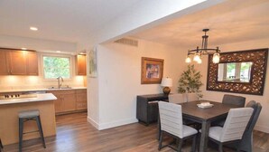 A modern kitchen with wooden cabinets, a dining area with a dark wooden table and chairs, and a decorative mirror on the wall. - Newly Updated in a Private Cove, With Firepit, Flat Lawn, Dock, Boat Slip & Kayaks in Osage Beach (Osage Beach)