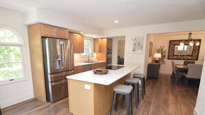 A modern kitchen with stainless steel appliances, a large island with stools, and a dining area with a chandelier. - Newly Updated in a Private Cove, With Firepit, Flat Lawn, Dock, Boat Slip & Kayaks in Osage Beach (Osage Beach)