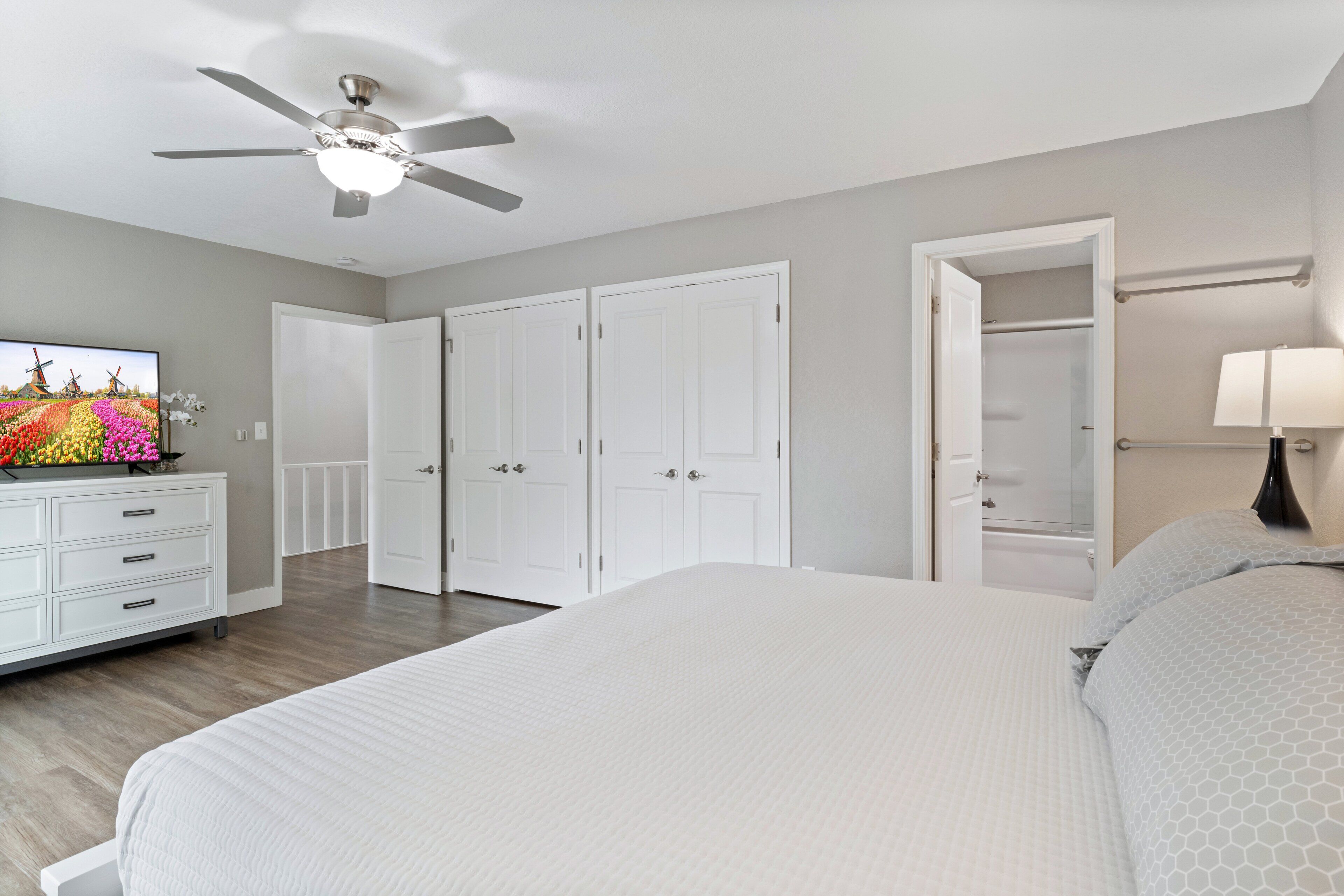 A bedroom with a bed, a ceiling fan, a dresser, a TV, and a closet.