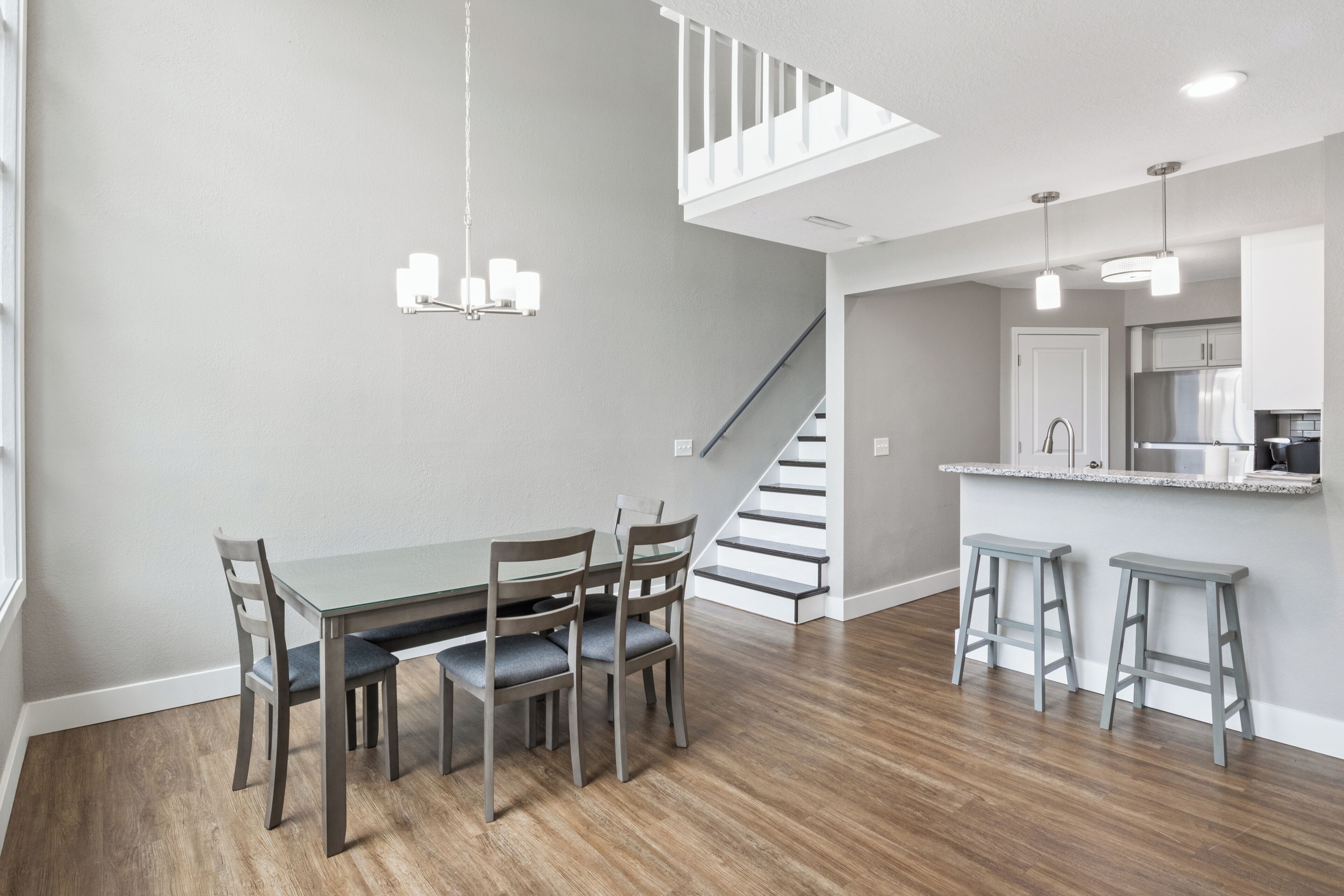 A modern kitchen with a built-in island, a dining area with a wooden table and chairs, and a staircase leading to an upper level.