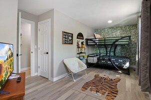 Un dormitorio con una cama litera, un televisor de pantalla plana, una silla y una alfombra con estampado de tigre.