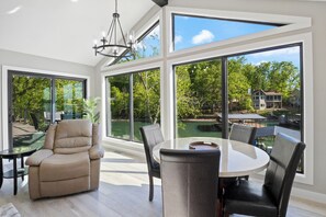 A spacious room with large windows, a comfortable reclining chair, a round table, and a view of a swimming pool and greenery. - Firepit, Hot Tub, Games In & Out, Spacious (Gravois Mills)