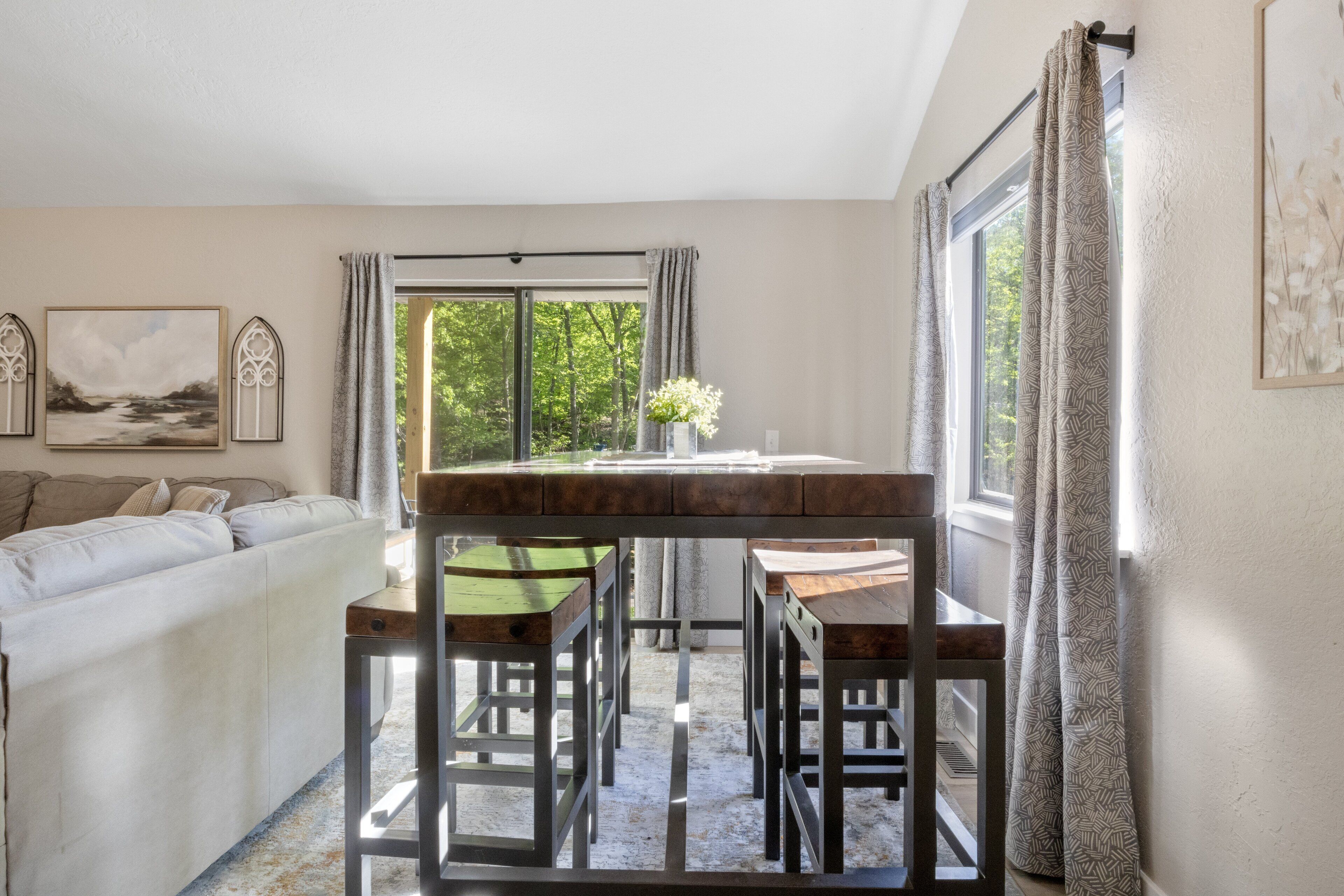 A cozy living room with a sofa, a dining table with chairs, and a view of greenery outside.