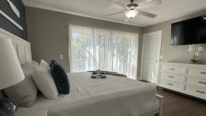 Une chambre à coucher comprenant un lit, une commode, un ventilateur de plafond et un téléviseur fixé au mur.