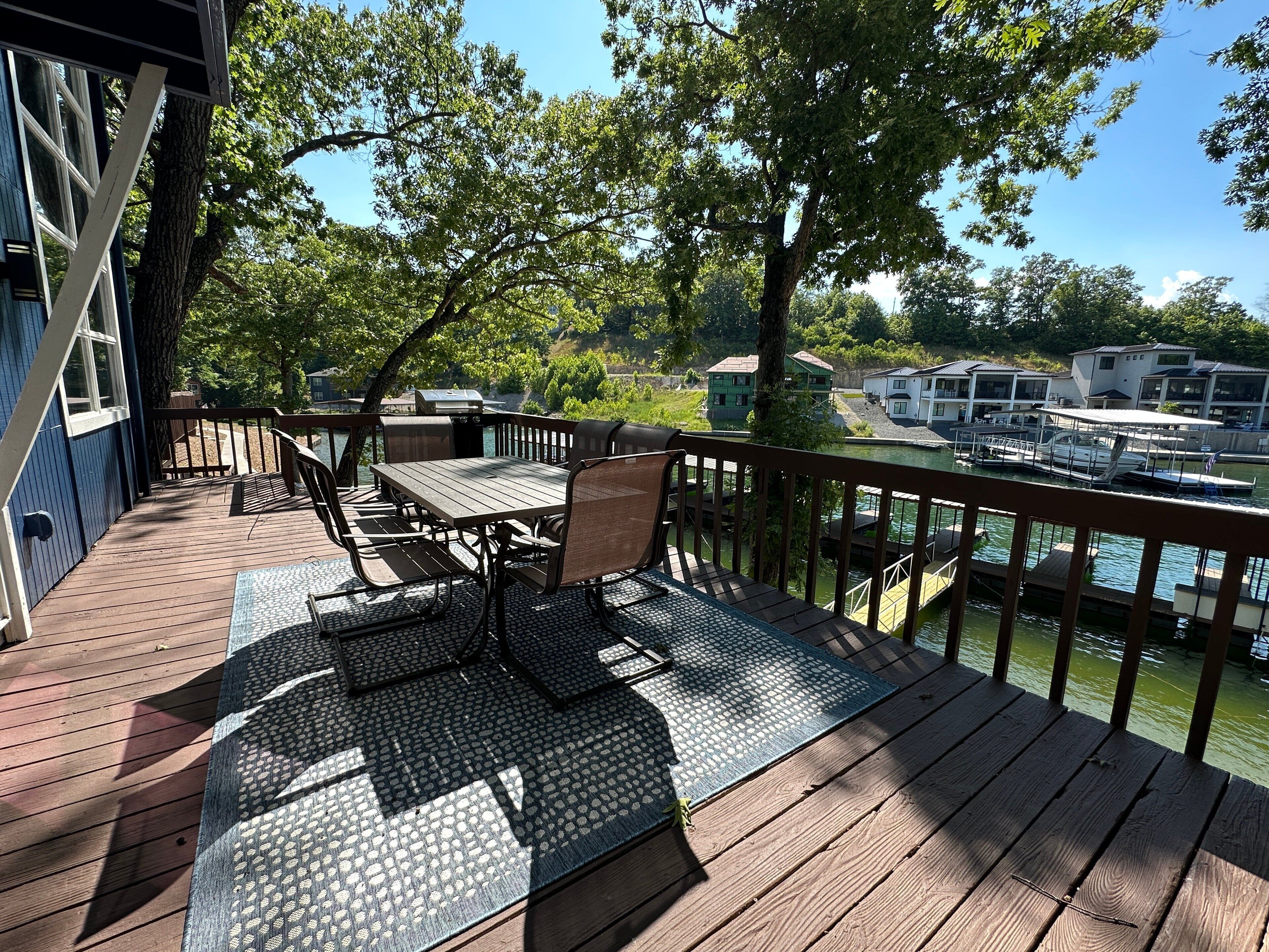 Terraza de madera con mesa y sillas, con vistas a un puerto deportivo con barcos y casas.
