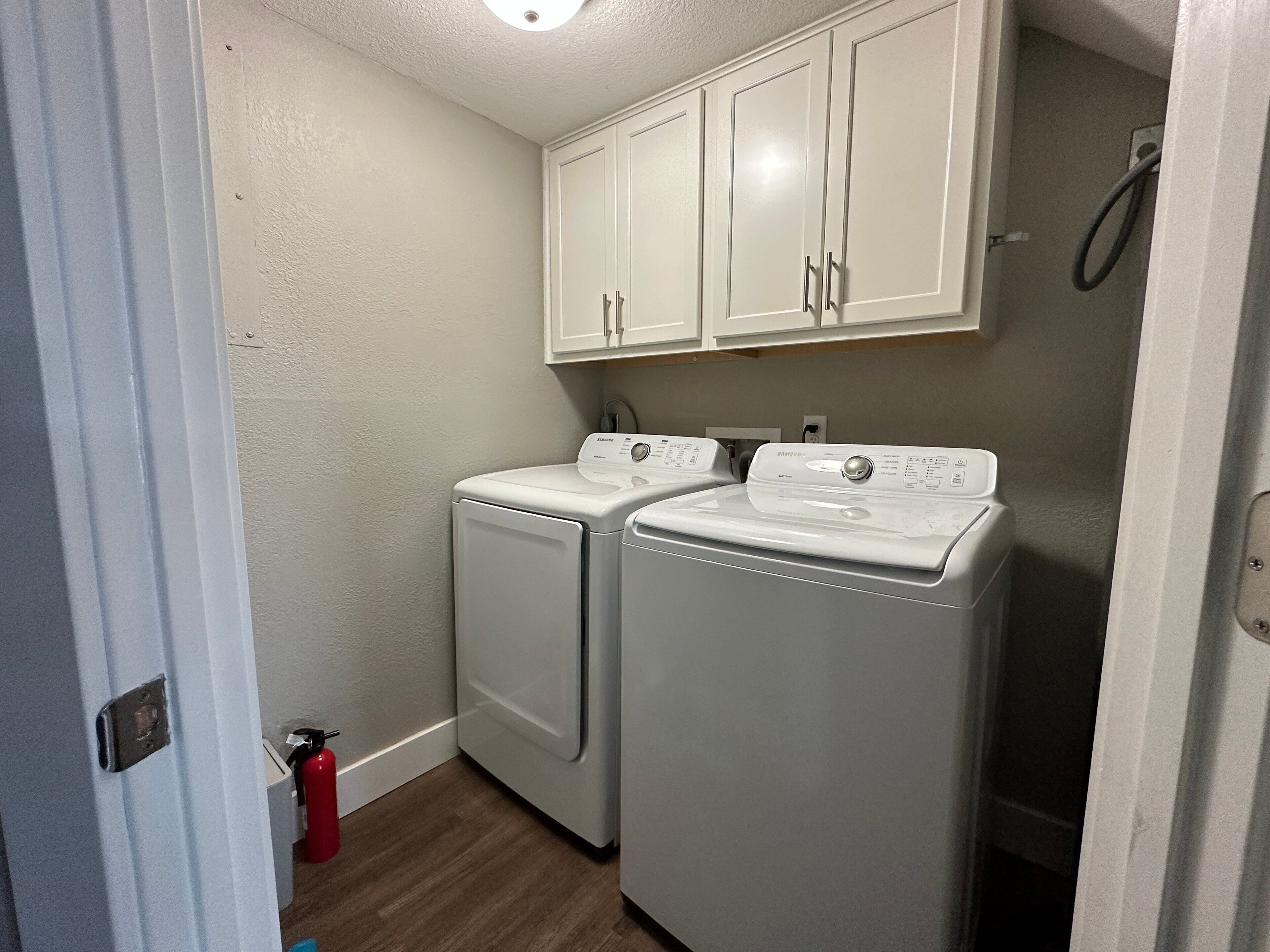 A laundry room with two front-loading washing machines, a white cabinet above, and a red fire extinguisher on the floor.