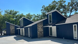 Une rangée de maisons modernes, bleues, avec des éléments en pierre et de grandes fenêtres, situées dans un quartier ensoleillé et bordé d’arbres.