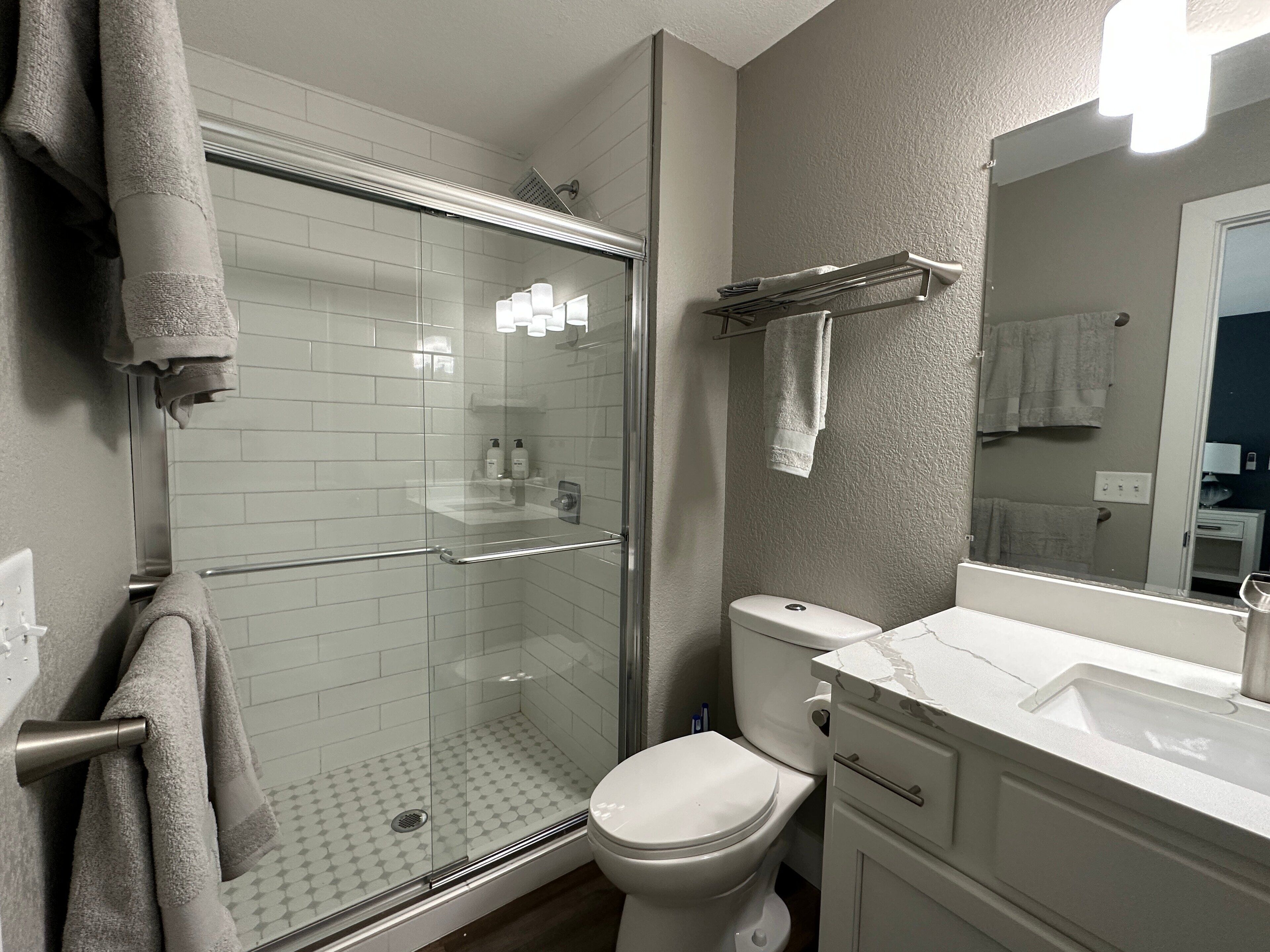 Un baño moderno con ducha envuelta en vidrio, inodoro blanco y lavamanos de mármol.
