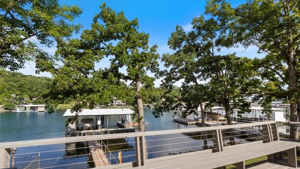 A wooden deck overlooking a lake with docked boats and a covered area. - Perfect Family House in Osage Beach With Expansive Deck, Private Dock, & Boat Slip (Osage Beach)