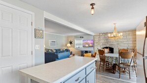 A kitchen with a marble countertop, a dining area with wooden chairs, a stone fireplace, and a television in the background. - Perfect Family House in Osage Beach With Expansive Deck, Private Dock, & Boat Slip (Osage Beach)