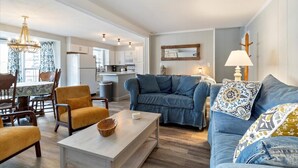 A spacious living room with a blue sofa, wooden coffee table, and a dining area with a patterned tablecloth. - Perfect Family House in Osage Beach With Expansive Deck, Private Dock, & Boat Slip (Osage Beach)