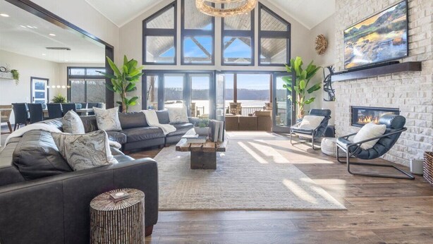 A spacious living room with a high ceiling, large windows, a fireplace, and a modern chandelier. - Loto Pointe, Updated Luxury Home w/ Boat & PWC Slip, Boat Ramp, Firepits, Pool Table & More! (Versailles)