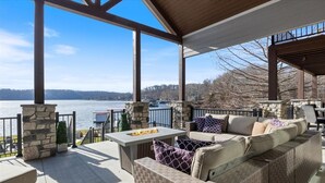 A covered outdoor seating area with stone pillars, a fire feature, and a view of a lake. - Loto Pointe, Updated Luxury Home w/ Boat & PWC Slip, Boat Ramp, Firepits, Pool Table & More! (Versailles)