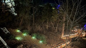 A wooden deck with a pathway, surrounded by trees and illuminated plants. - Amazing Views Close to the Strip - Private Dock! (Lake Ozark)
