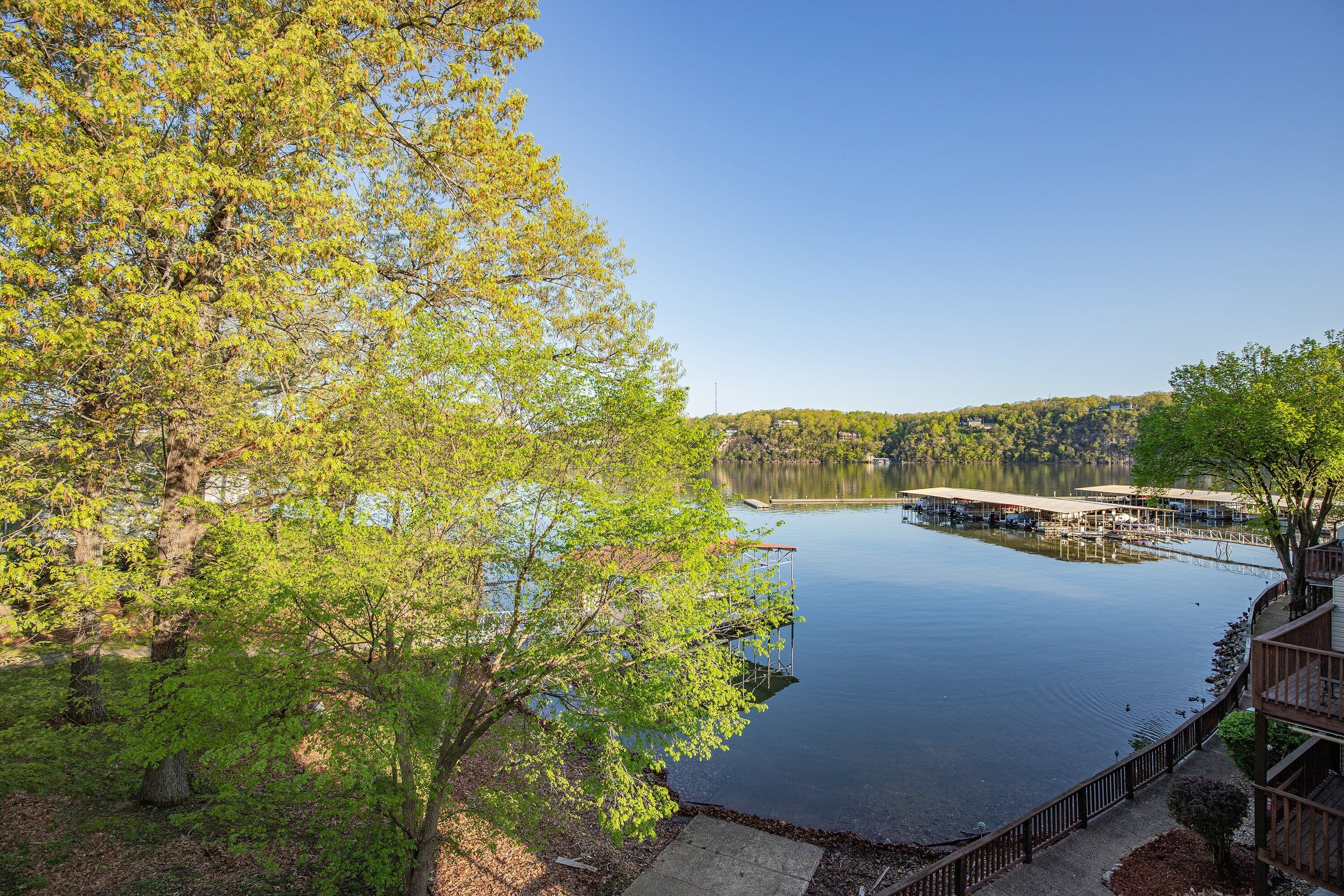 Vista sobre un lago con barcos amarrados, una terraza de madera y zona boscosa.