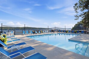 Ein Swimmingpool mit blauen Liegestühlen und Blick auf eine bewaldete Landschaft.