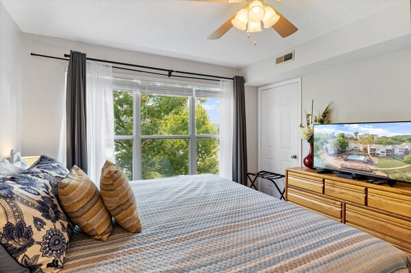 A bedroom with a large bed, a television on a wooden dresser, and a window with curtains. - Dream Condo With Perfect Location for All The Fun! (Osage Beach)