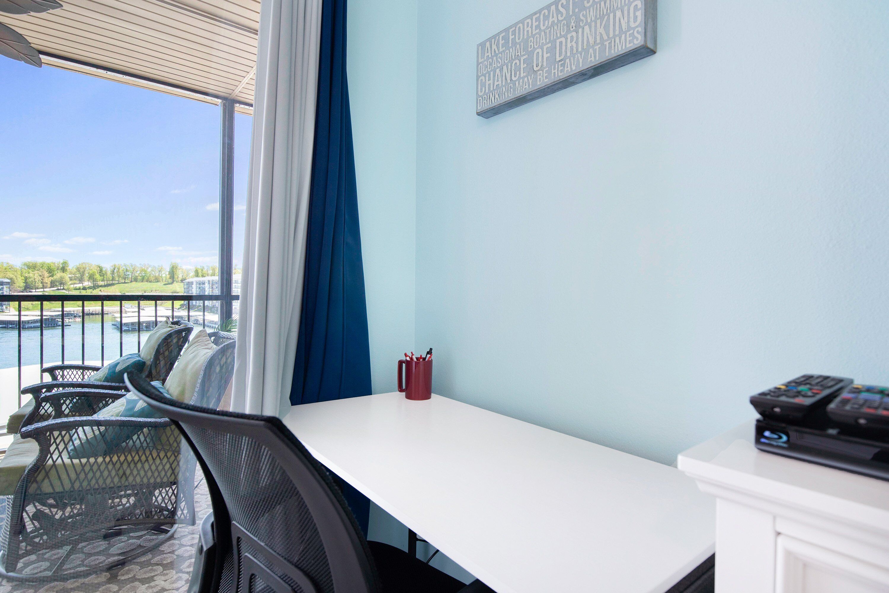 Una habitación con vista a un cuerpo de agua, una mesa blanca, una taza roja y un control remoto sobre un mueble blanco.