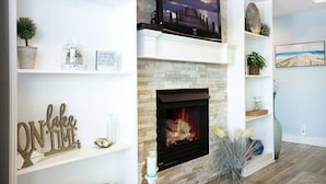 Un salon avec une cheminée, des étagères ornées de plantes, un téléviseur et un tableau accroché au mur.